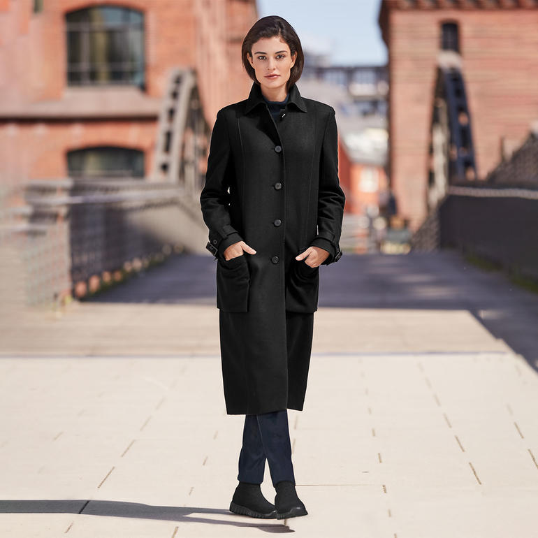 Femme en manteau noir avec des bottes tricotées sur un pont.