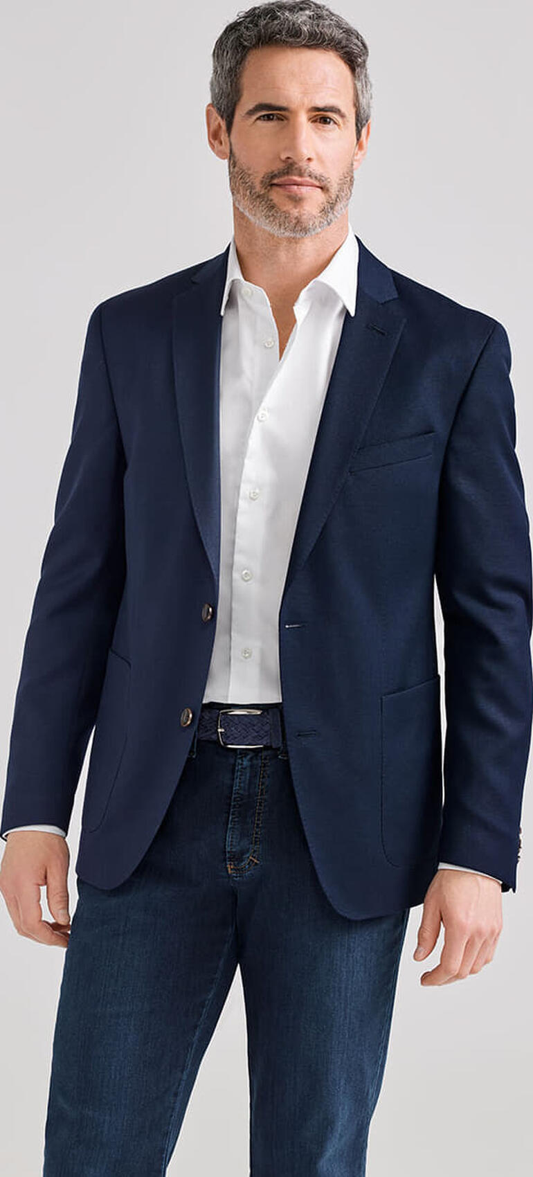 Homme en veste de voyage sombre avec chemise blanche, pose décontractée.
