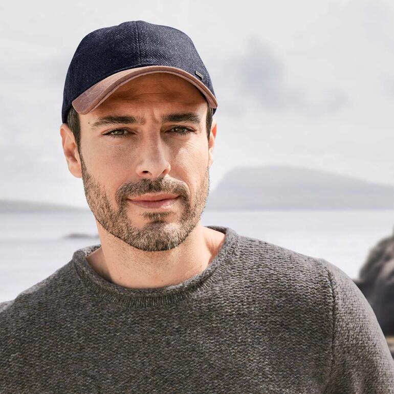 Homme portant un pull de pêcheur avec une casquette bleu foncé, regardant un paysage aquatique.