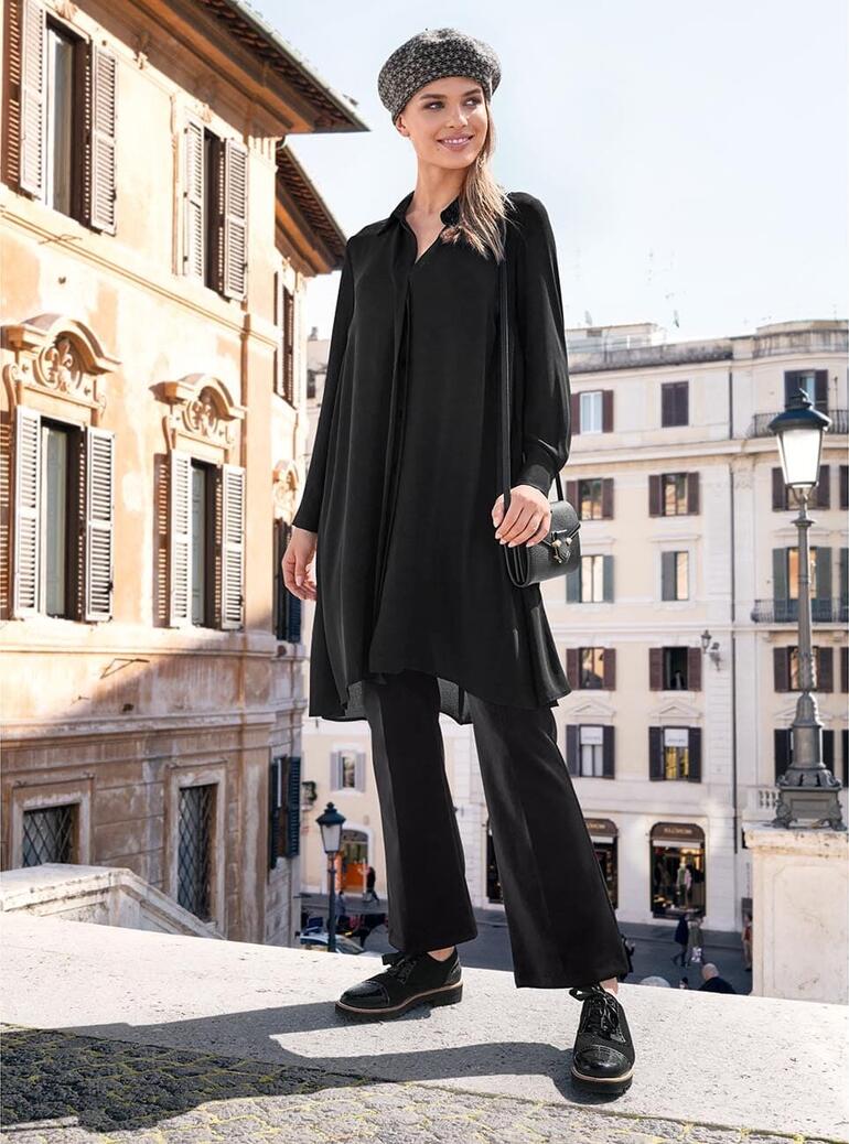 Blouse longue Janice & Jo Femme en blouse noire longue, portant un chapeau sur des marches dans une ville.