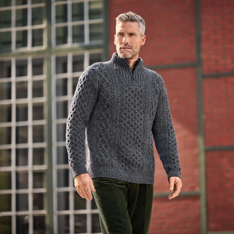 Homme portant un pull IrelandsEye Aran gris avec motif en relief dans un environnement urbain.
