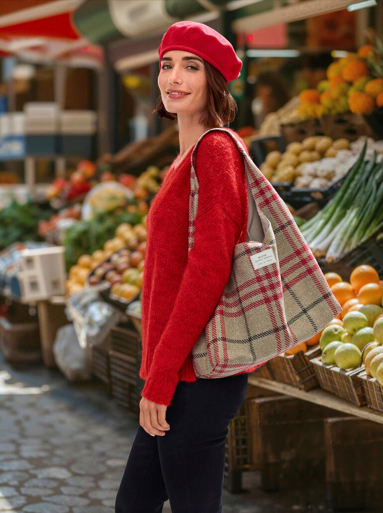 Femme portant un béret en coton rouge et un pull rouge, se tenant sur un marché.