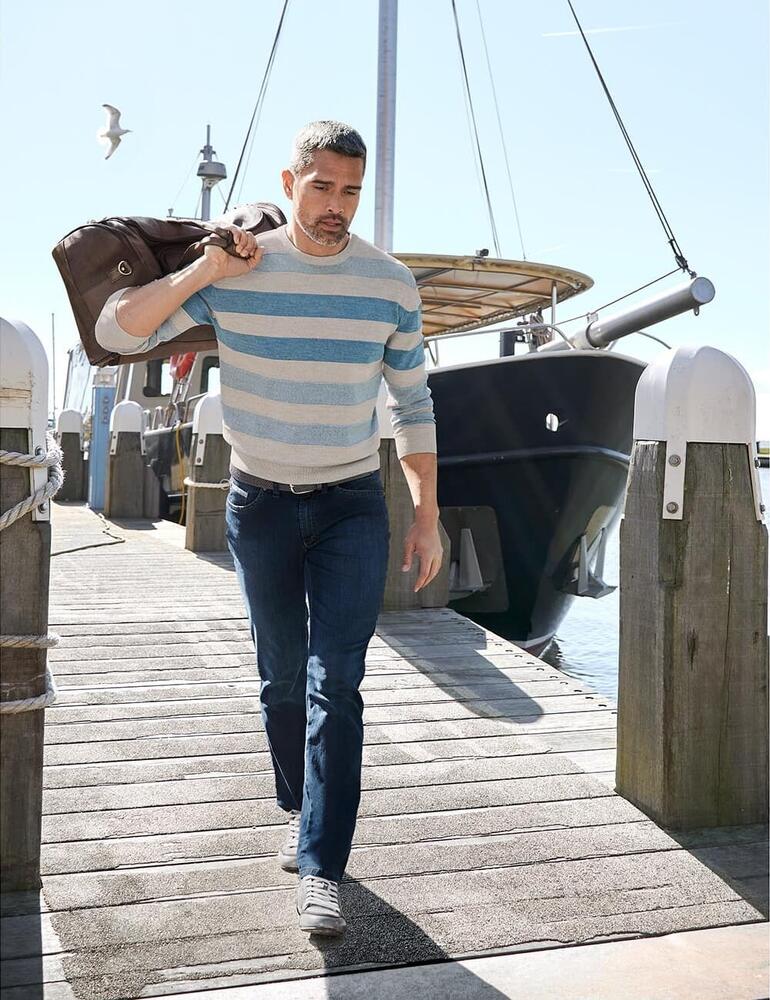 Pull rayé Tom Ripley dans un cadre maritime avec un sac et un jean.