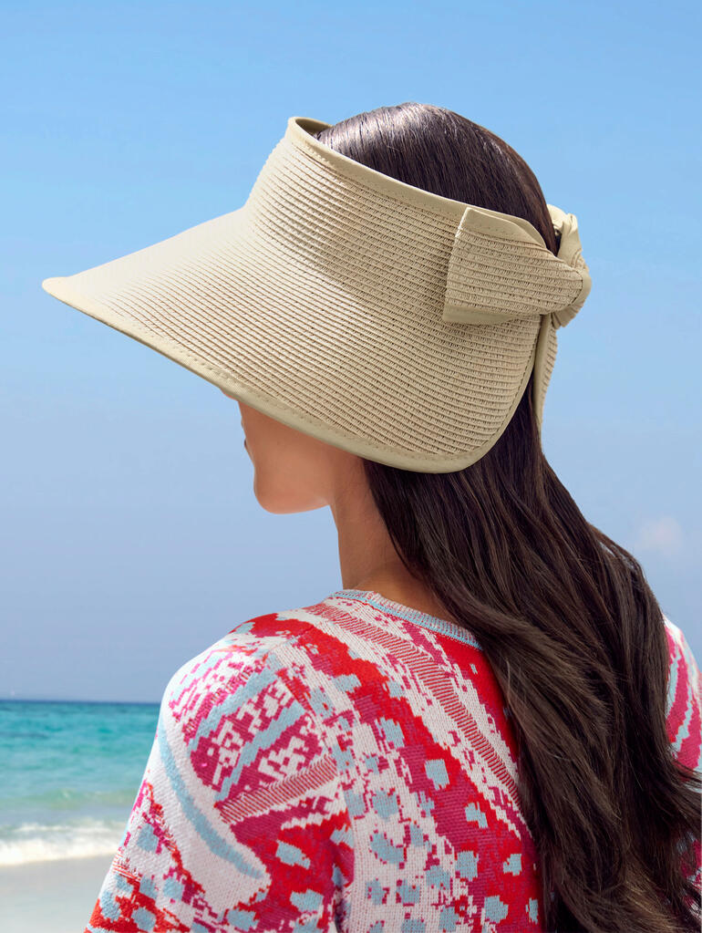 Femme avec un chapeau en papier regarde latéralement vers la plage.
