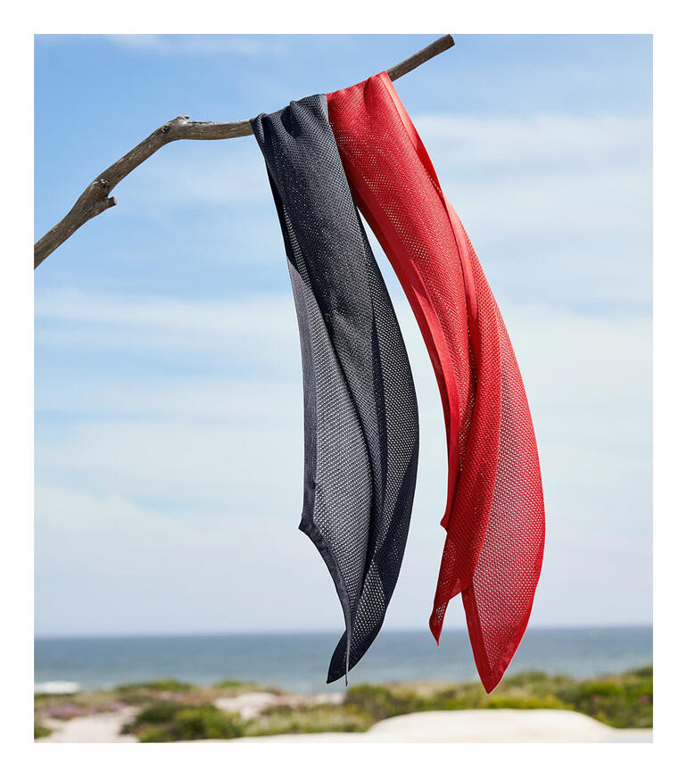 Écharpe en soie tricotée noire et rouge accrochée à une branche sur la plage.