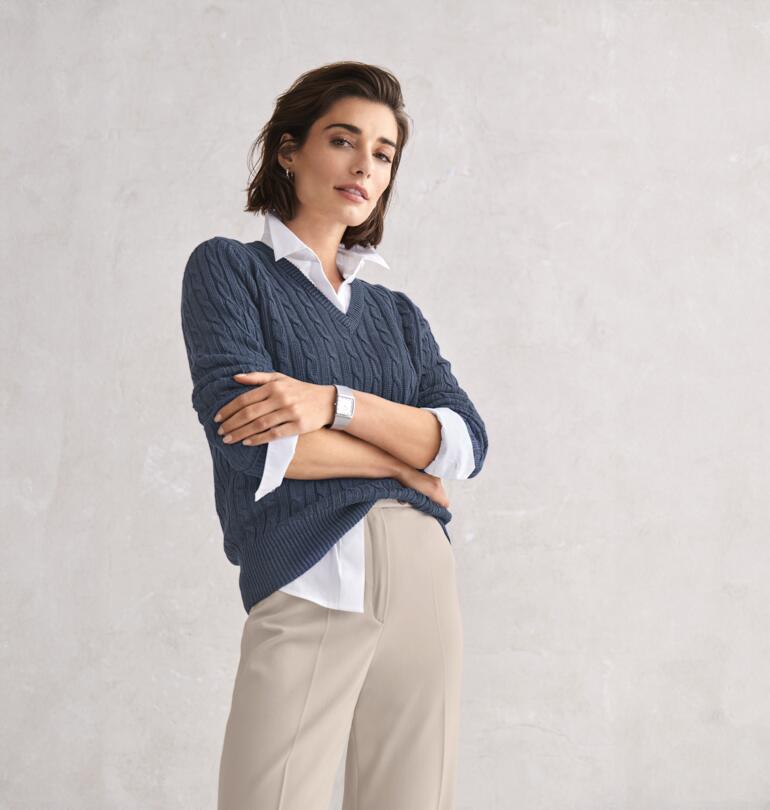 Femme posant dans un pull en lin gris Carbery et un pantalon beige.