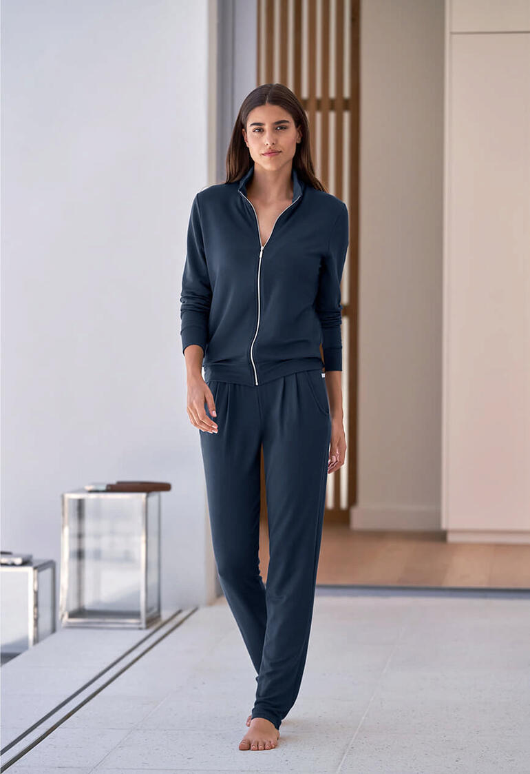 Femme en ensemble modal bleu marine avec fermeture éclair marchant dans une pièce claire.