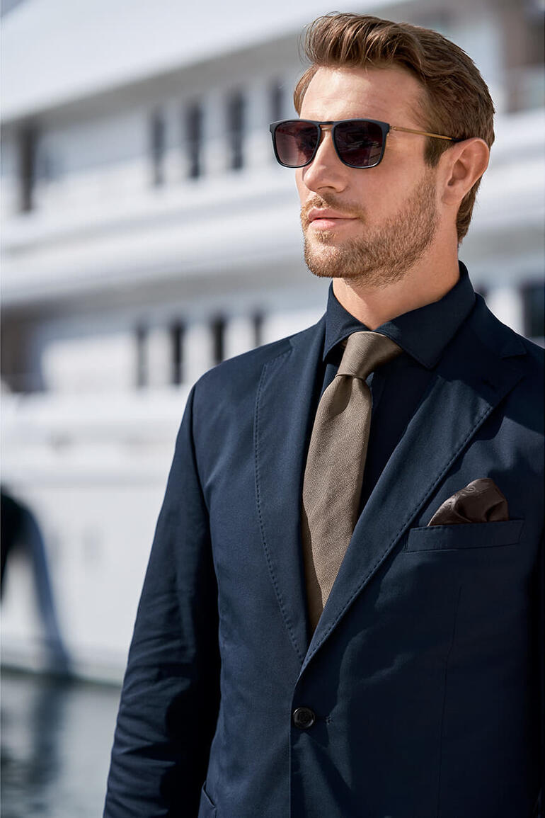 Marron Homme en costume avec une cravate olive foncée et des lunettes de soleil.