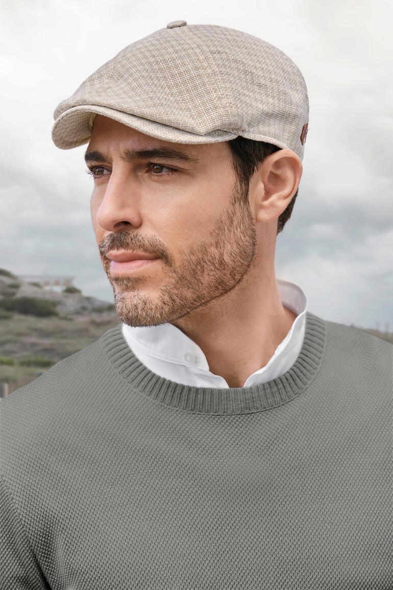 Homme portant une casquette claire avec un pull gris