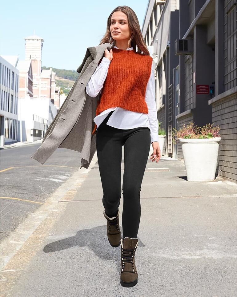 Bootines à lacets en cuir dʼagneau Chaaya Femme portant un pull orange et un manteau gris marche sur le trottoir avec des bottes.