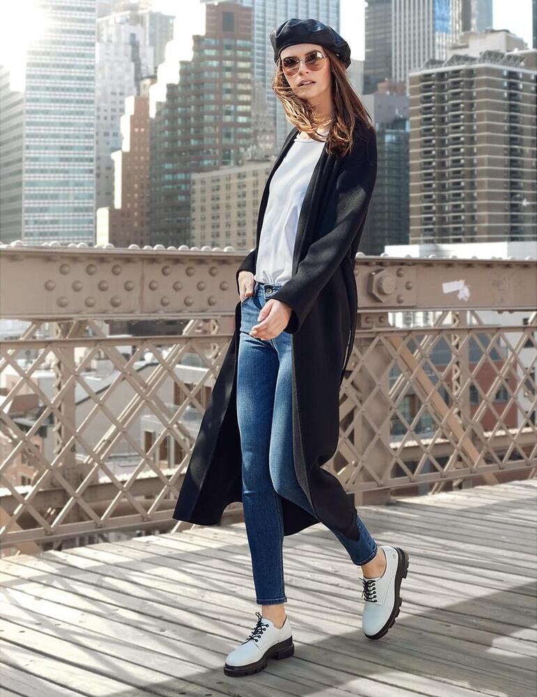 Blanc Modèle en manteau noir avec jean dans un paysage urbain.