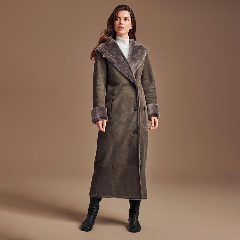 Femme en manteau réversible en peau de mouton gris avec grand col se tient sur un fond beige.