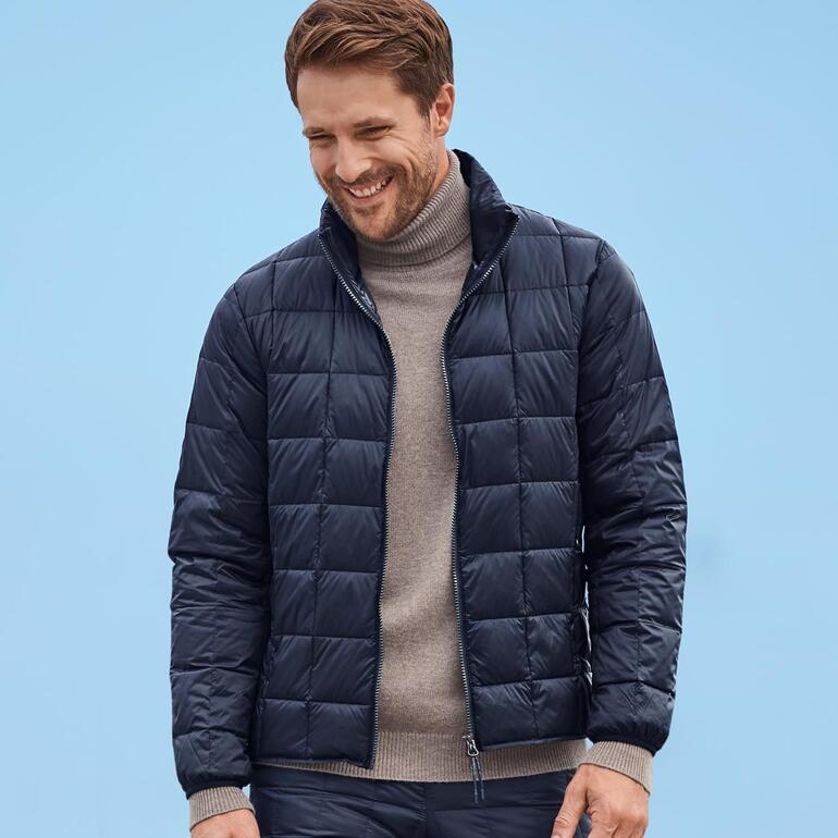 Homme souriant en doudoune marine devant un fond bleu.