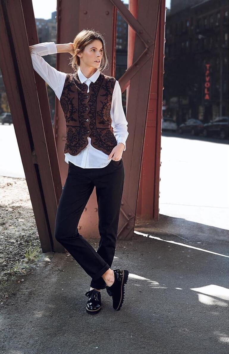 Femme portant un gilet à ornements d'alpaga et un pantalon noir, posant avec audace en ville.