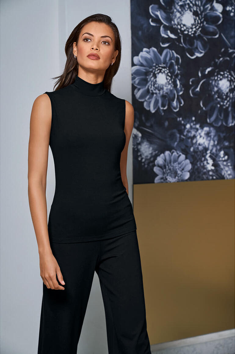 Femme en haut sans manches noir avec col montant devant un graphique floral.