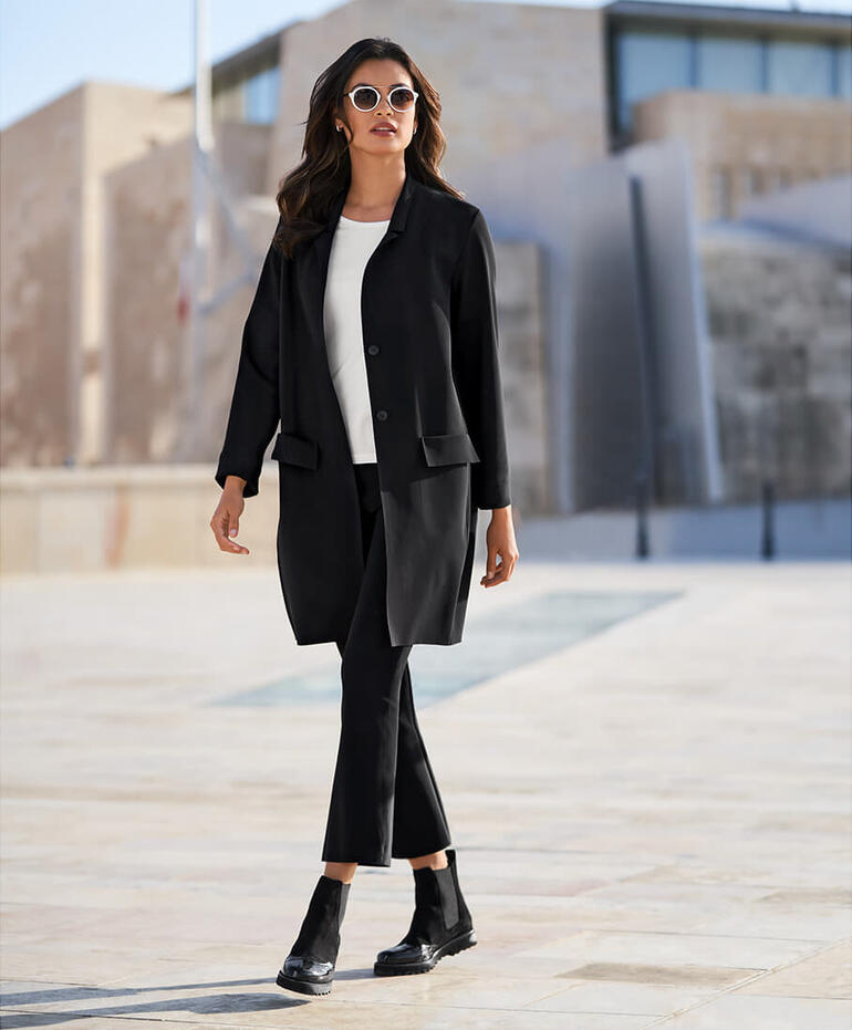 Femme portant un blazer-manteau noir dans un environnement urbain.