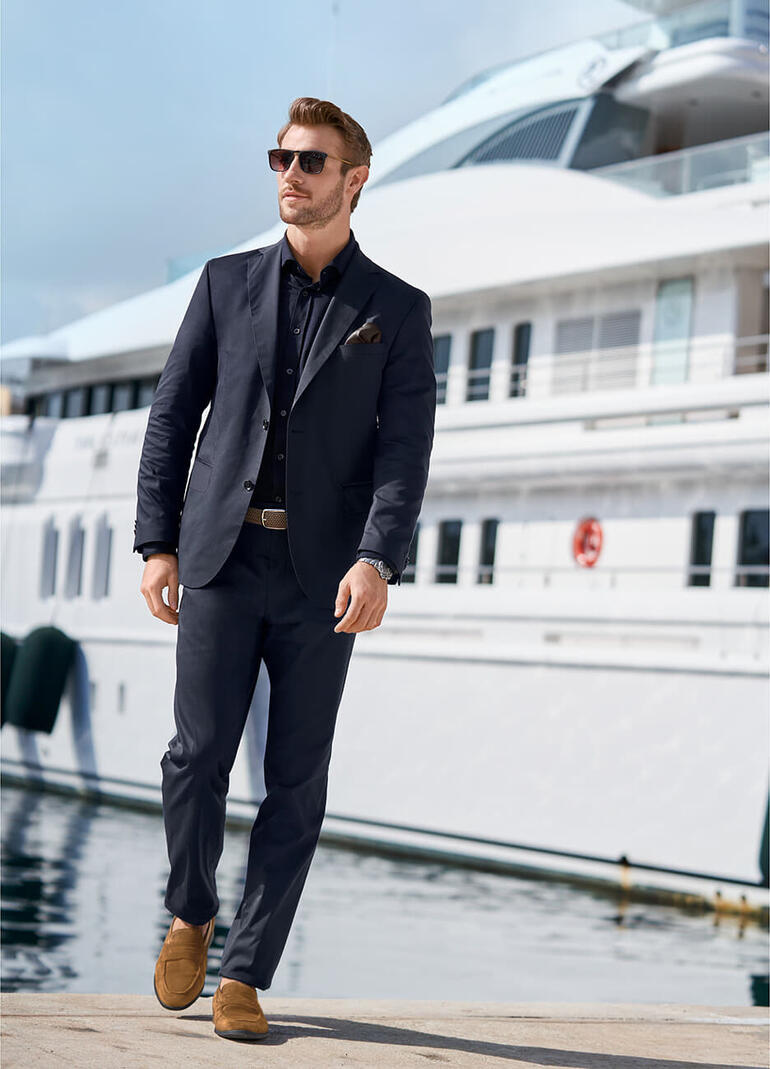 Veste et Pantalon, Bleu Homme en costume sombre devant un yacht de luxe.