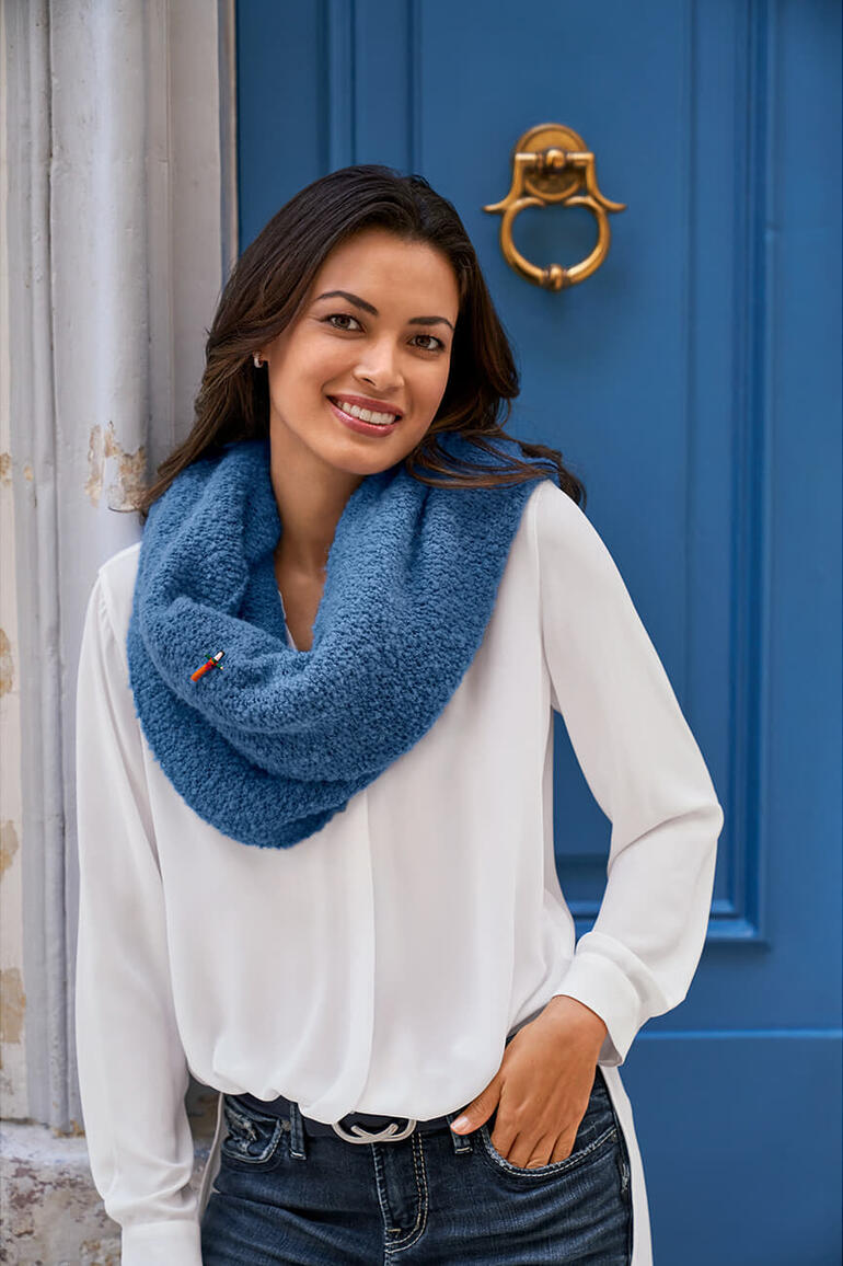 Blanc Femme portant une blouse blanche avec un poncho en bouclé bleu devant un mur bleu