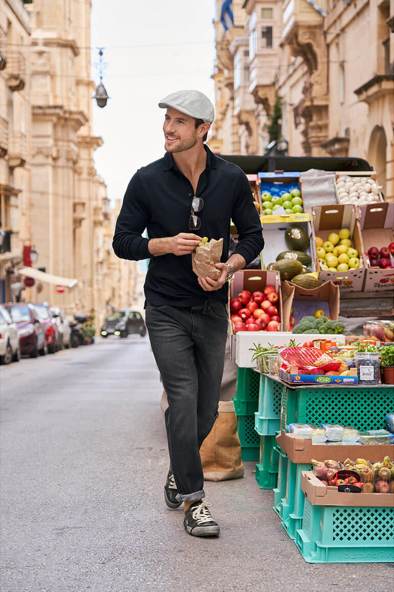 Homme portant une casquette Seersucker de Bailey of Hollywood sur un marché en plein air, tenant un sac de nourriture.