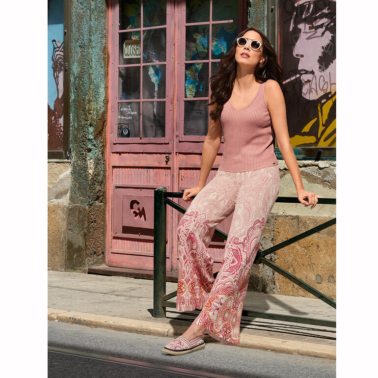 Espadrilles en tricot Ivko Femme en haut rose et pantalons colorés assise devant un mur coloré.