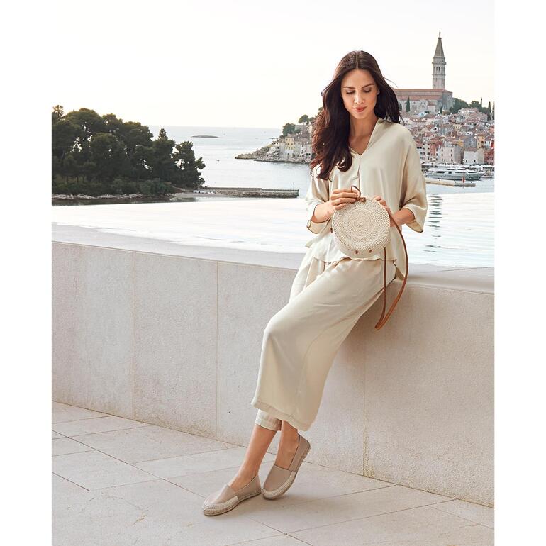 Beige Femme assise sur un mur, portant des vêtements clairs et des espadrilles en cuir.