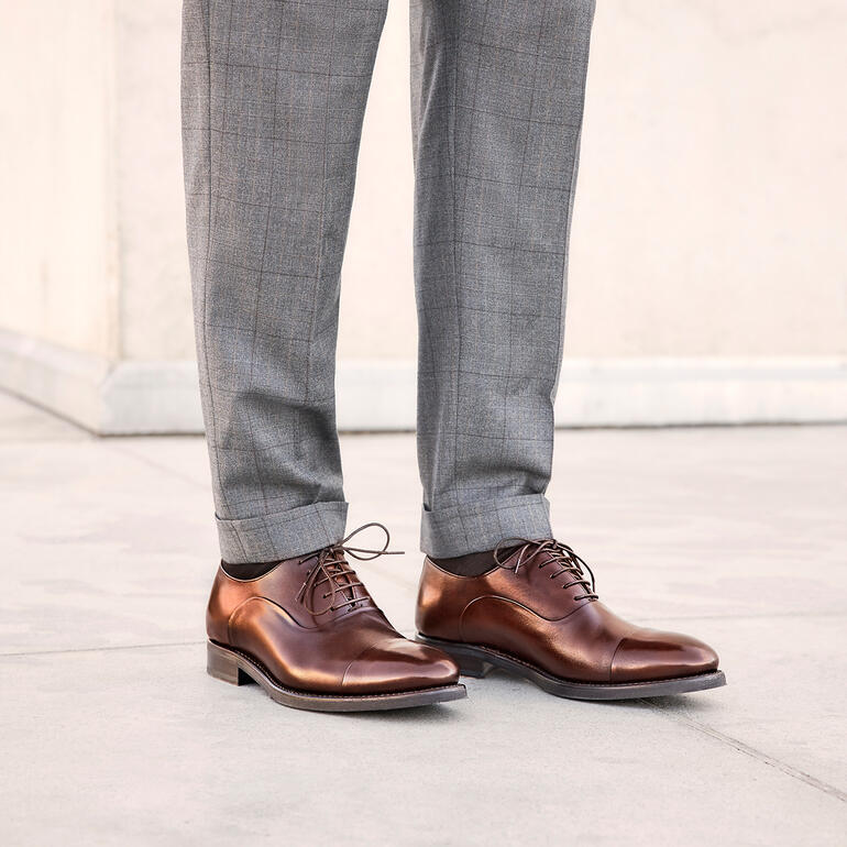 Homme en pantalon gris et chaussures Cordwainer business marron debout avec le dessus du pied ouvert.