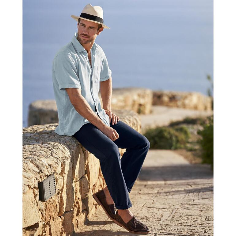 Homme en chemise en lin vintage assis sur un mur au bord de la mer