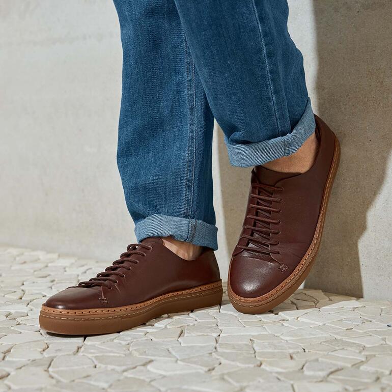 Homme portant des sneakers en cuir marron avec un jean sur un sol clair.