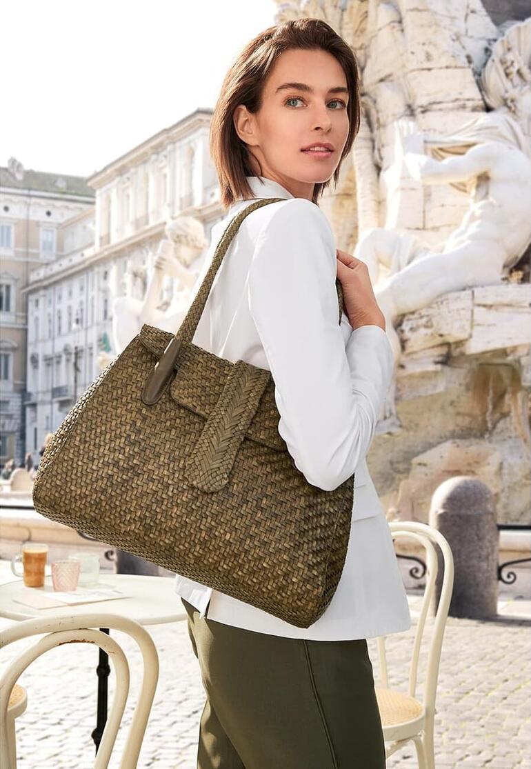 Femme portant un sac en cuir tressé Allan K en vert olive devant un décor historique