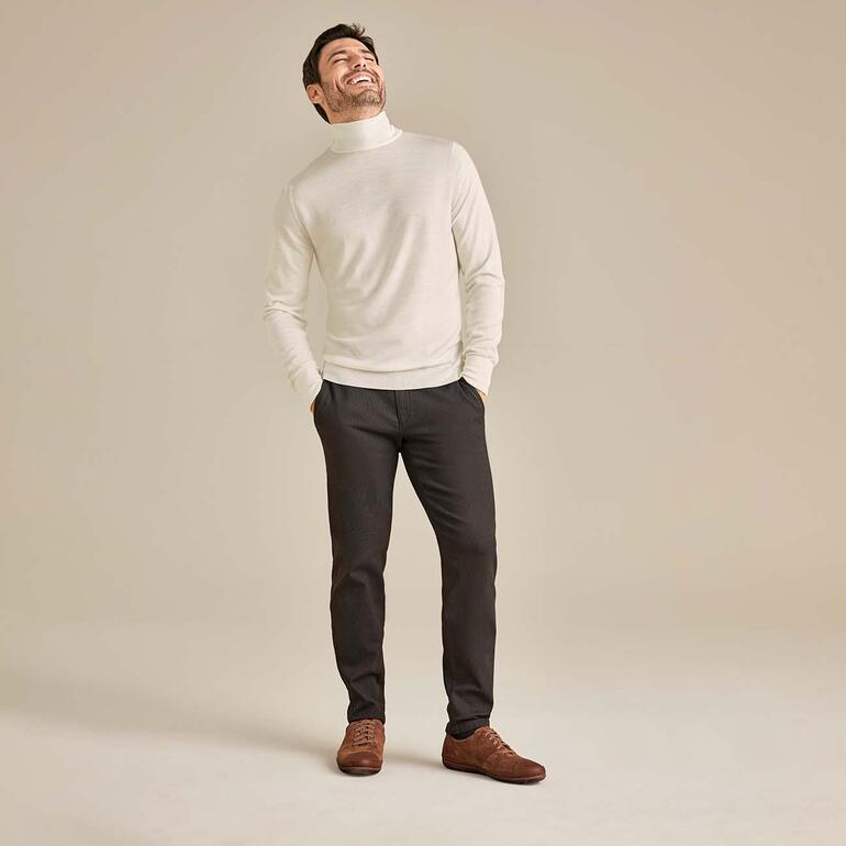 Chino hivernal 24h Brax Homme en pull à col roulé blanc et pantalon gris, souriant.