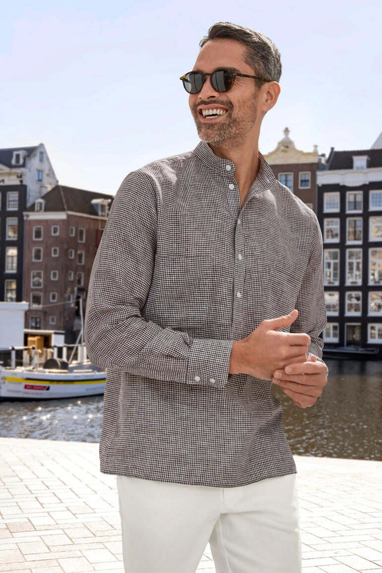 Homme souriant en chemise en lin Nehru à carreaux devant l'eau en ville.