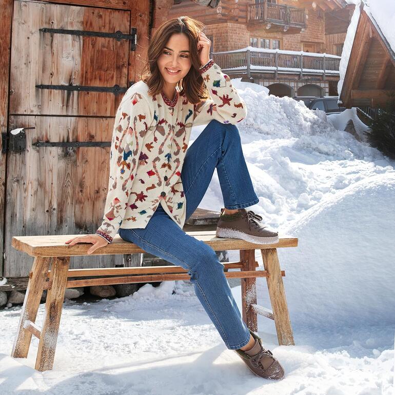 Femme en cardigan en alpaga à motifs floraux, assise sur un banc en bois dans la neige