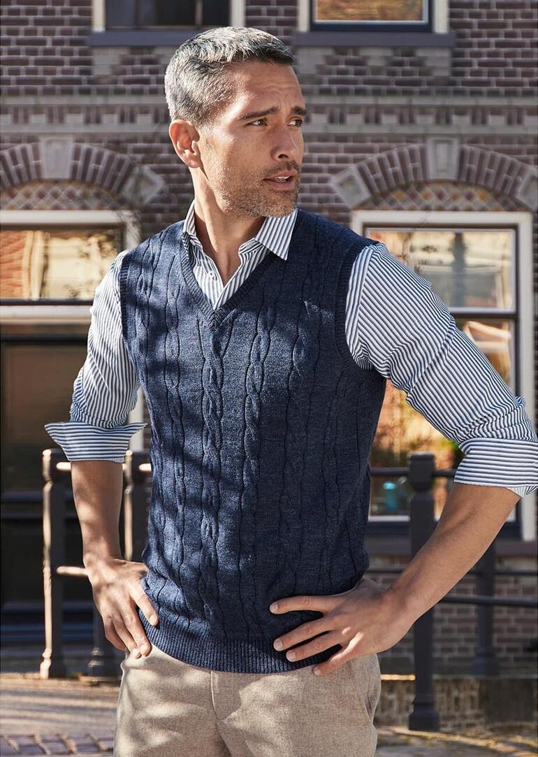 Homme portant un pull en maille noire sur une chemise, se tenant détendu.