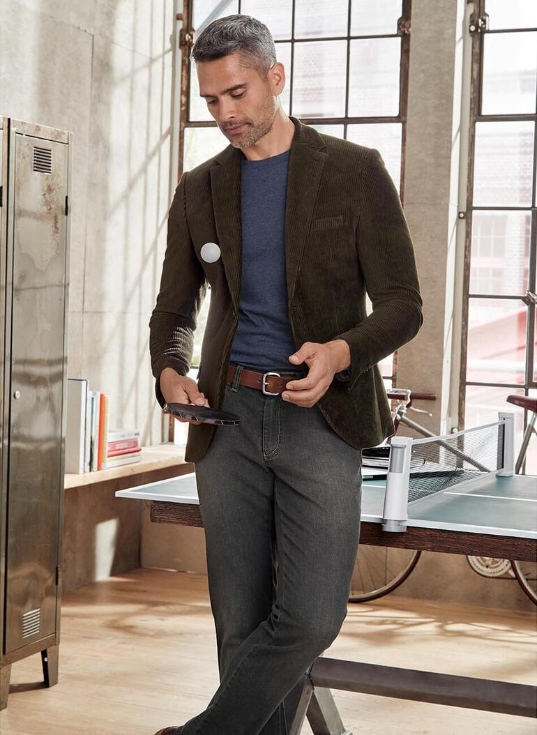 Marine Homme en blazer et T-shirt, regardant un smartphone, à côté d'une table avec des accessoires.