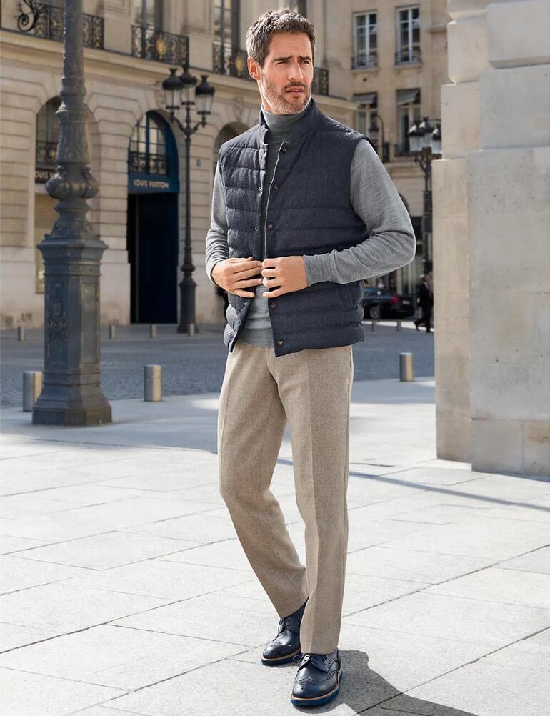 Gris Homme en gilet matelassé gris sur une place avec des bâtiments élégants.