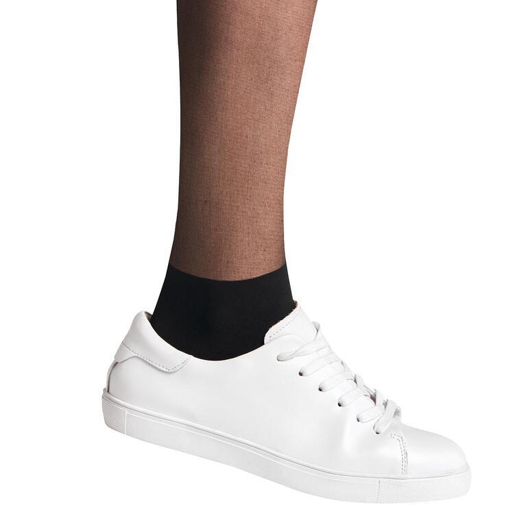 Gros plan d'un pied portant une basket blanche et des collants Falke noirs.