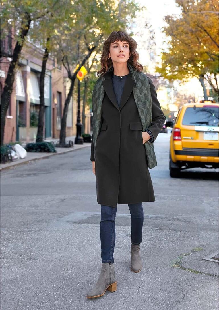 Noir/Gris/Anthracite Femme portant un manteau long et une veste verte marchant dans une rue de ville.