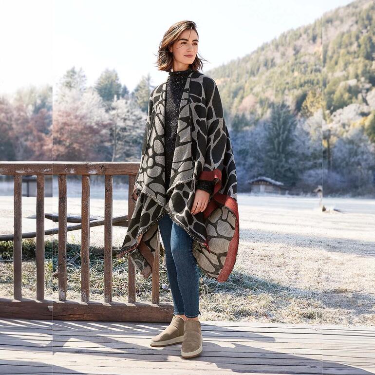 Poncho réversible Ancini Poncho réversible Ancini avec différents motifs, porté par une femme dans un paysage enneigé.