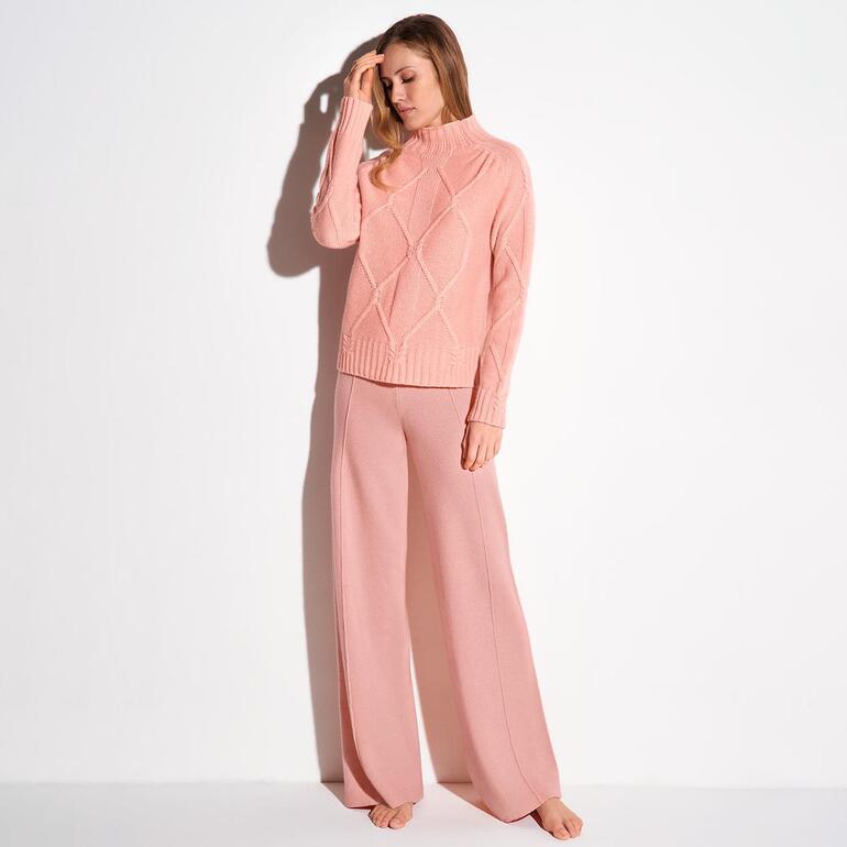 Femme portant un pull rose et un pantalon Marlene devant un fond neutre.