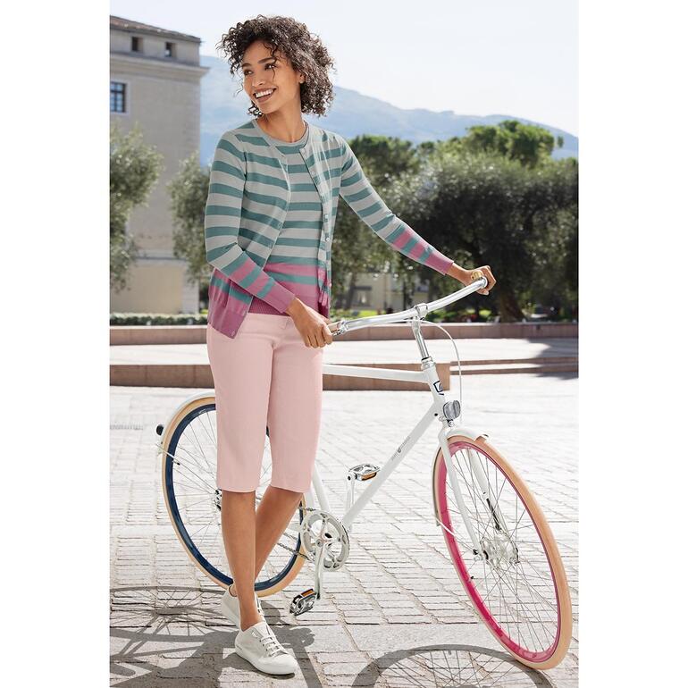 Bleu/Rose Femme en haut rayé et pantalon rose, debout à côté d'un vélo.
