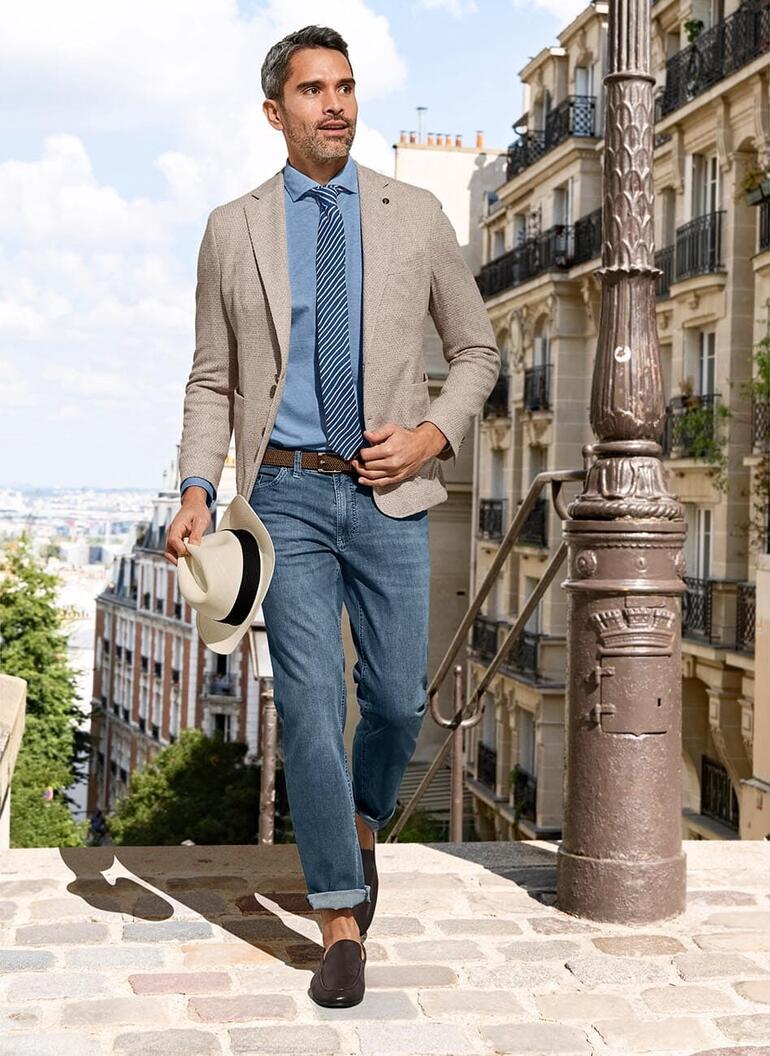 Brun foncé Homme portant un polo en Supima, dans un environnement urbain avec un blazer, une cravate à rayures et un chapeau.