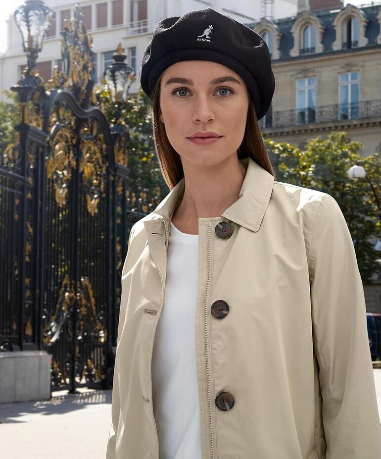Noir Femme portant un béret en bambou Kangol et un blazer beige dans un environnement urbain.
