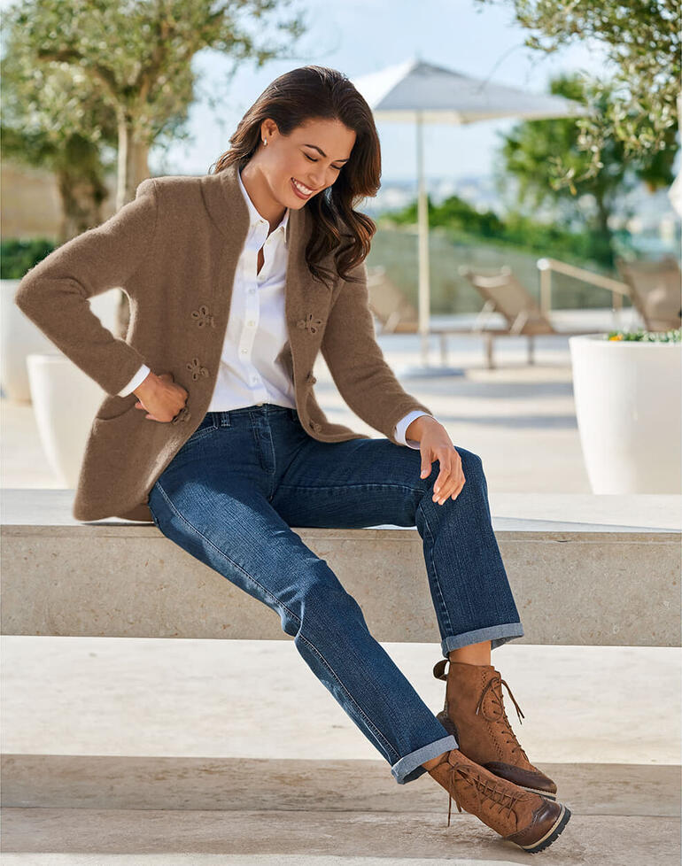 Femme en veste Softwalk marron de Mirabell, assise détendue sur un banc en pierre.