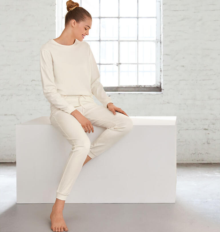 Femme en pyjama claire de Natural, assise et souriante sur une assise blanche.