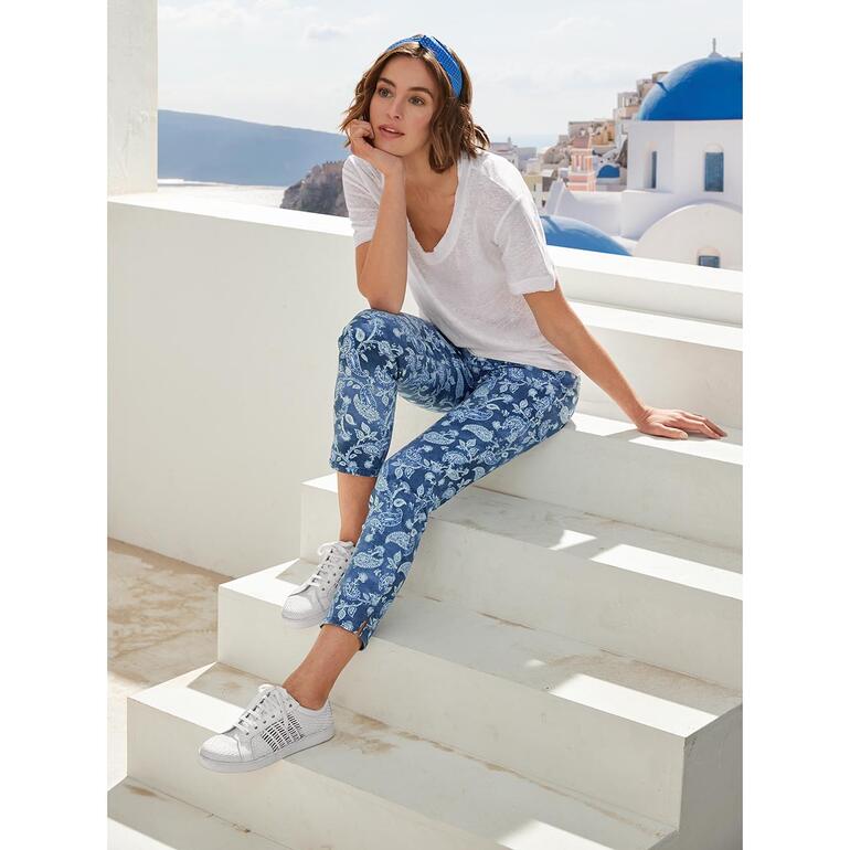 Pantalon 5 poches magique paisley RAPHAELA-BY-BRAX Femme assise sur des marches en pantalon paisley bleu et t-shirt blanc.