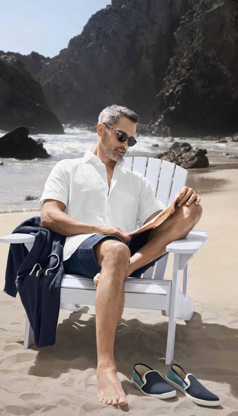 Homme en chemise seersucker assis calmement sur une chaise à la plage.
