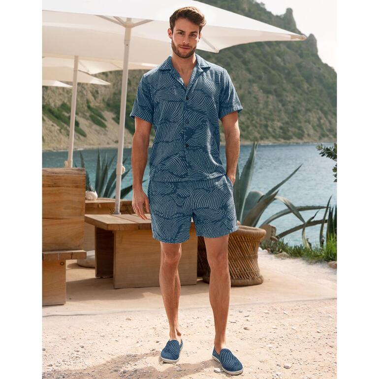 Homme en chemise en éponge rayée et shorts se tient sur la plage