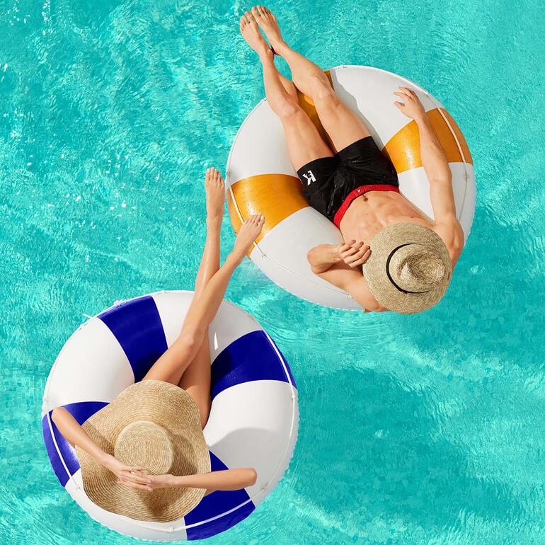 Couple dans l'eau avec des chapeaux en paille Zahati Wave sur des bouées de piscine.