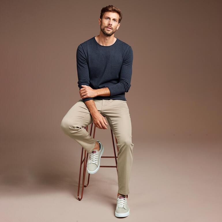 Bleu jean Homme assis sur un tabouret, portant un pull bleu marine et un pantalon clair.