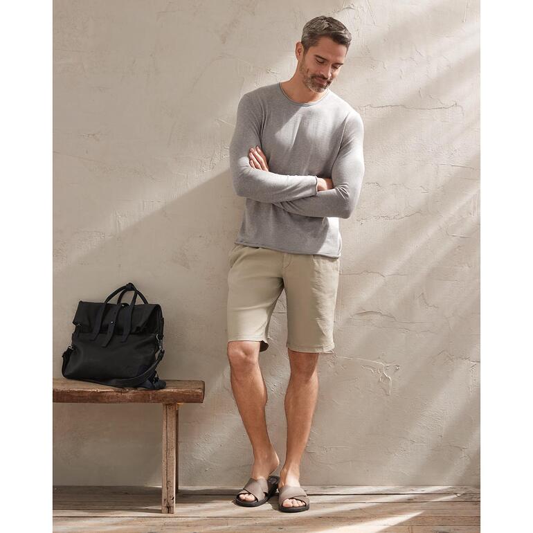 Beige Homme portant un short beige clair et un pull gris, se tenant devant un mur.